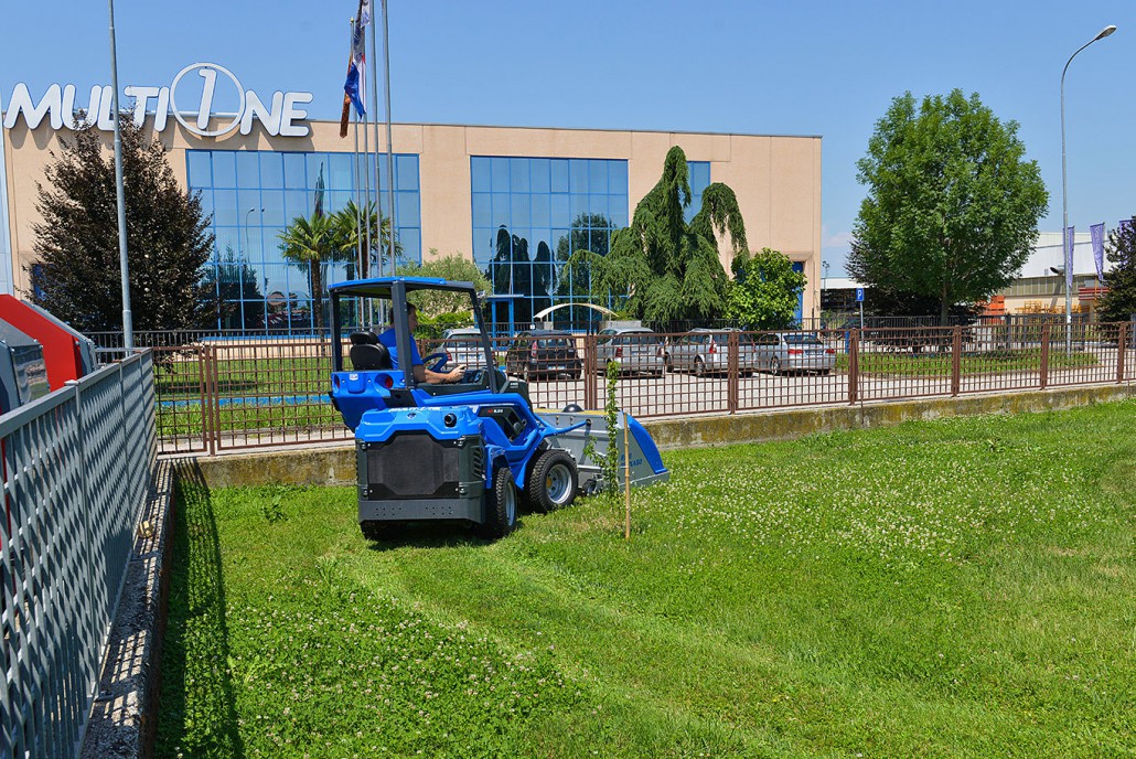 MultiOne mini loader 6 series with tornado lawn mower on a grass field in front of multione venue