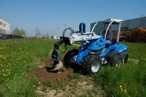 auger for tree with bucket in action in a field
