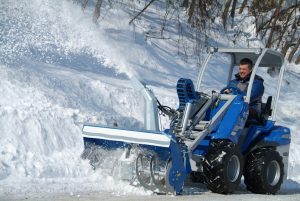 snow blower cleaning a snow-covered street; the driver on the miniloader visibly happy.