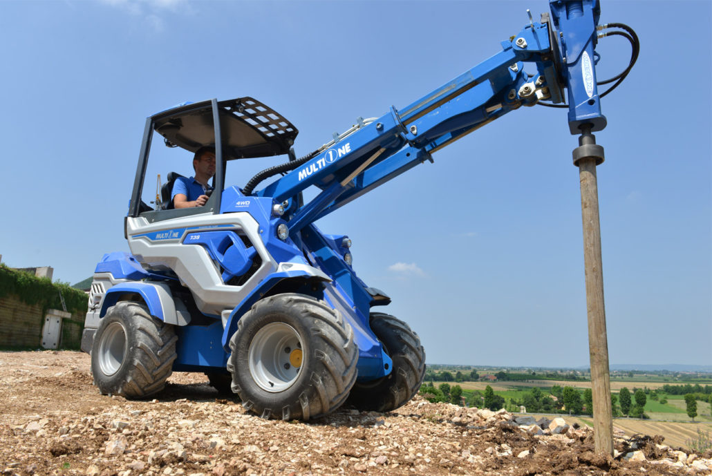 worker driving a mini loader with a stake planter on a
